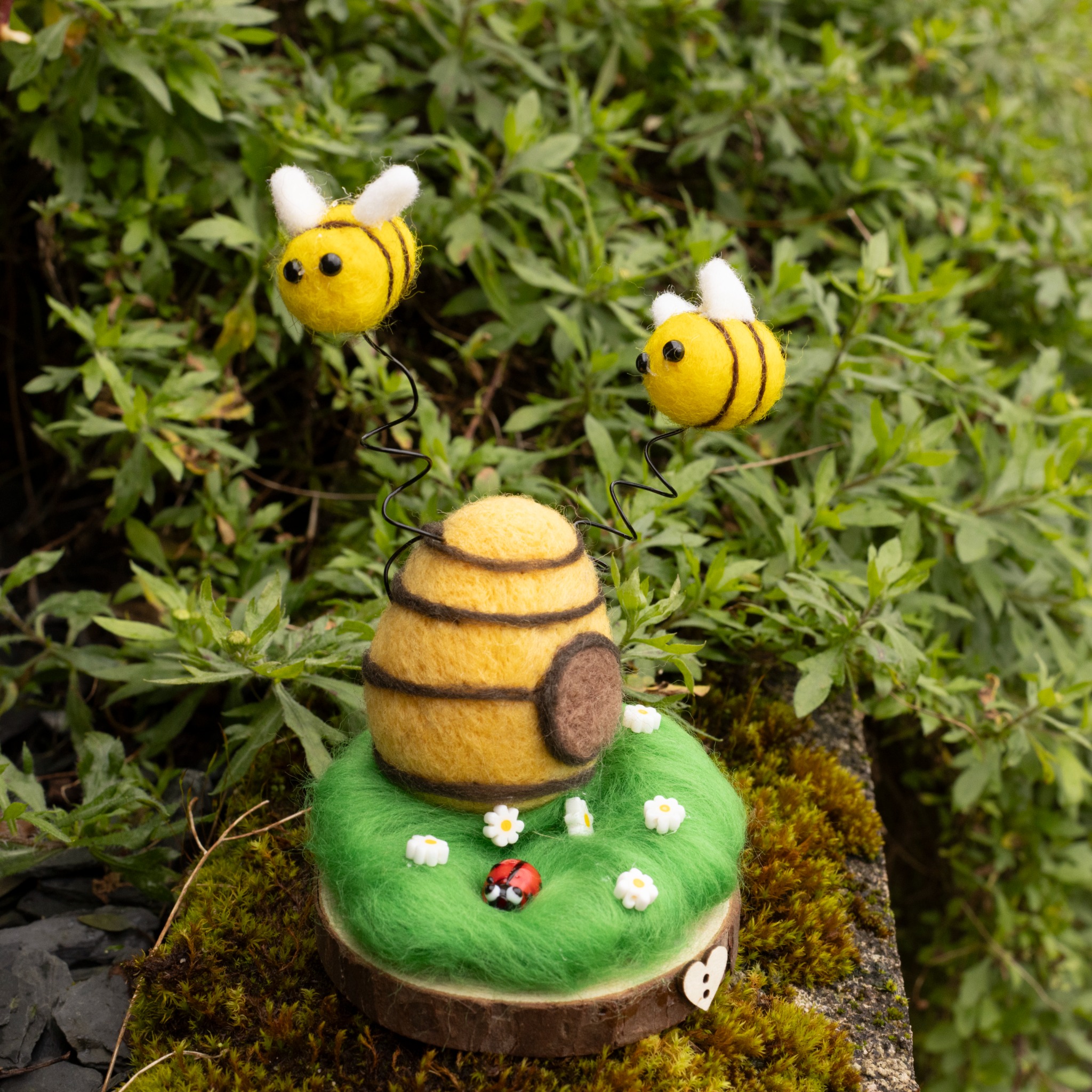 Needle-felted beehive with two bees hovering above on springs.